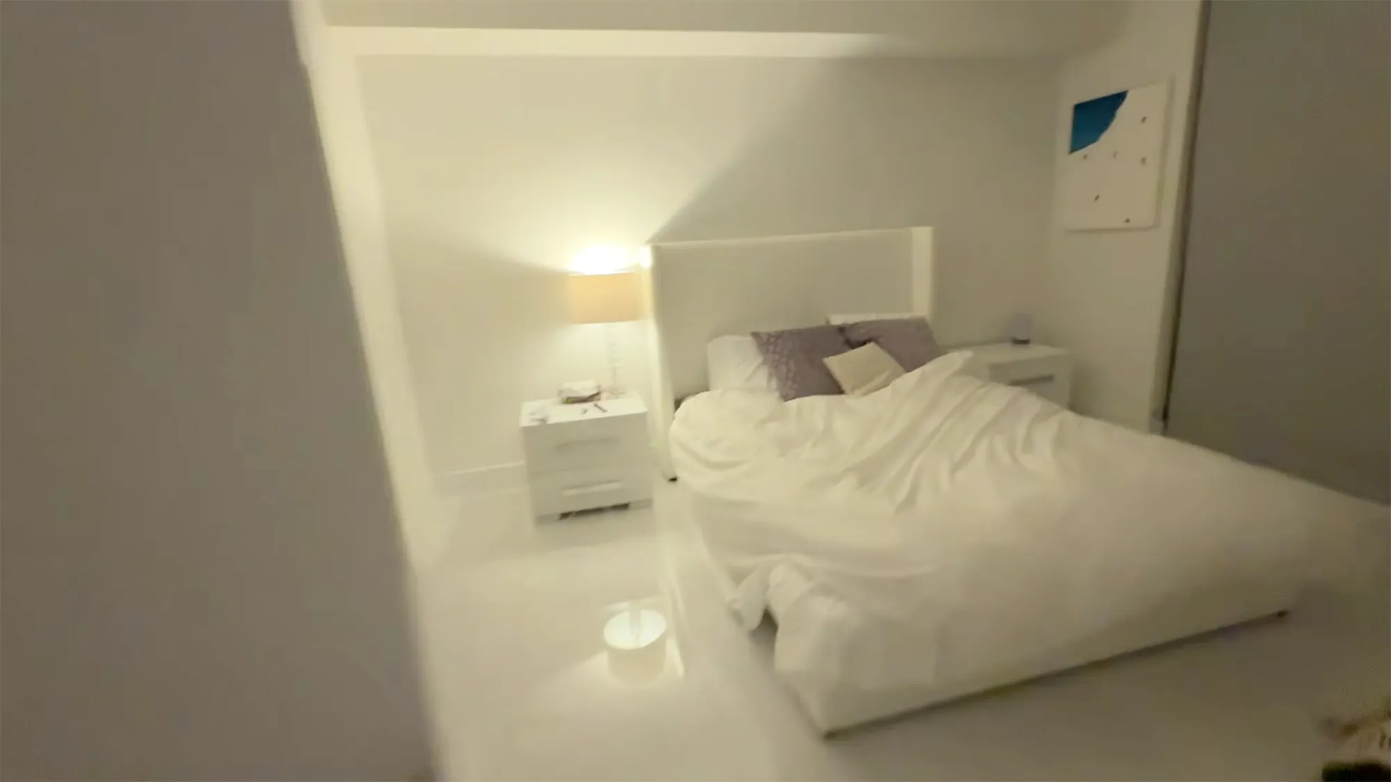Bedroom with white bed and nightstands, lamp, and abstract art.