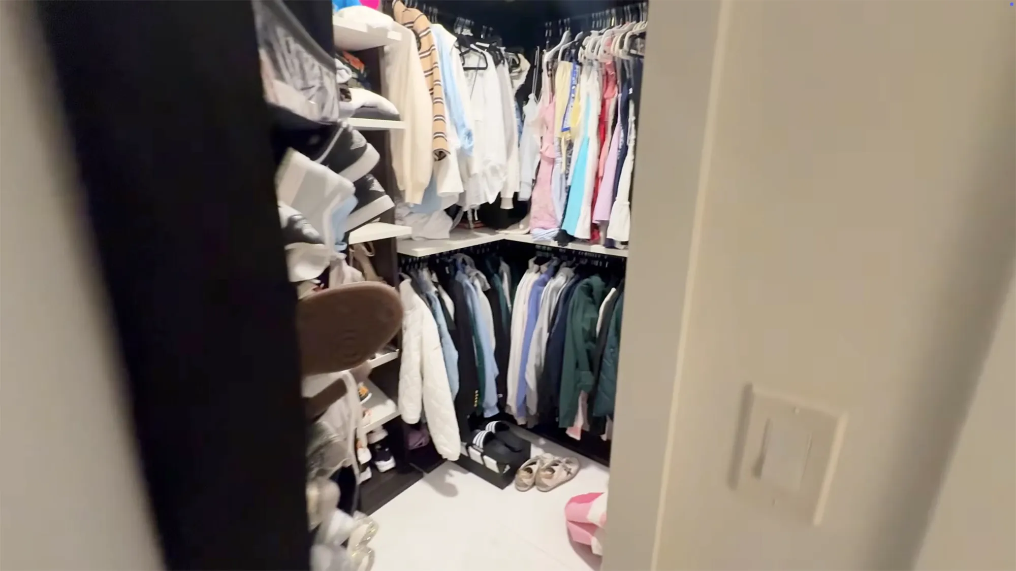 Walk-in closet with clothes hanging on racks and shoes on shelves.