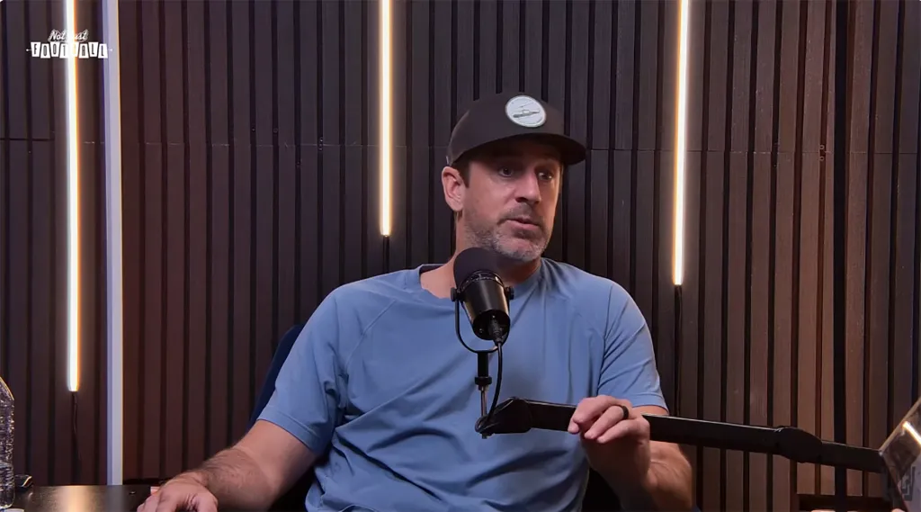 Aaron Rodgers speaks into a microphone at a podcast.