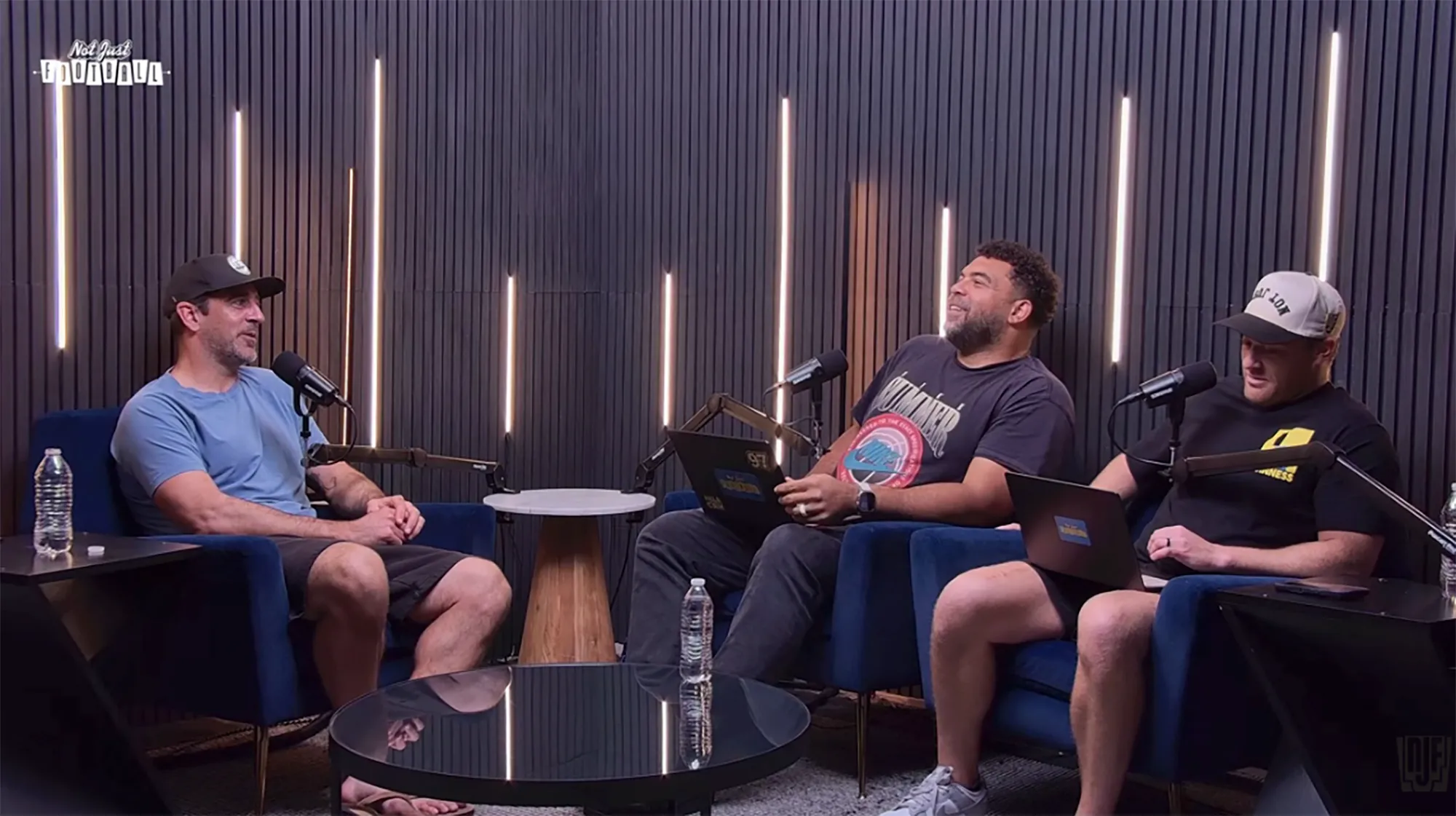Three men on a podcast, sitting in blue armchairs, talking into microphones.