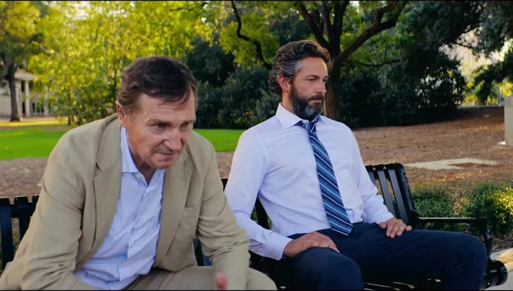 Zachary Levi and Liam Neeson sitting on a park bench.