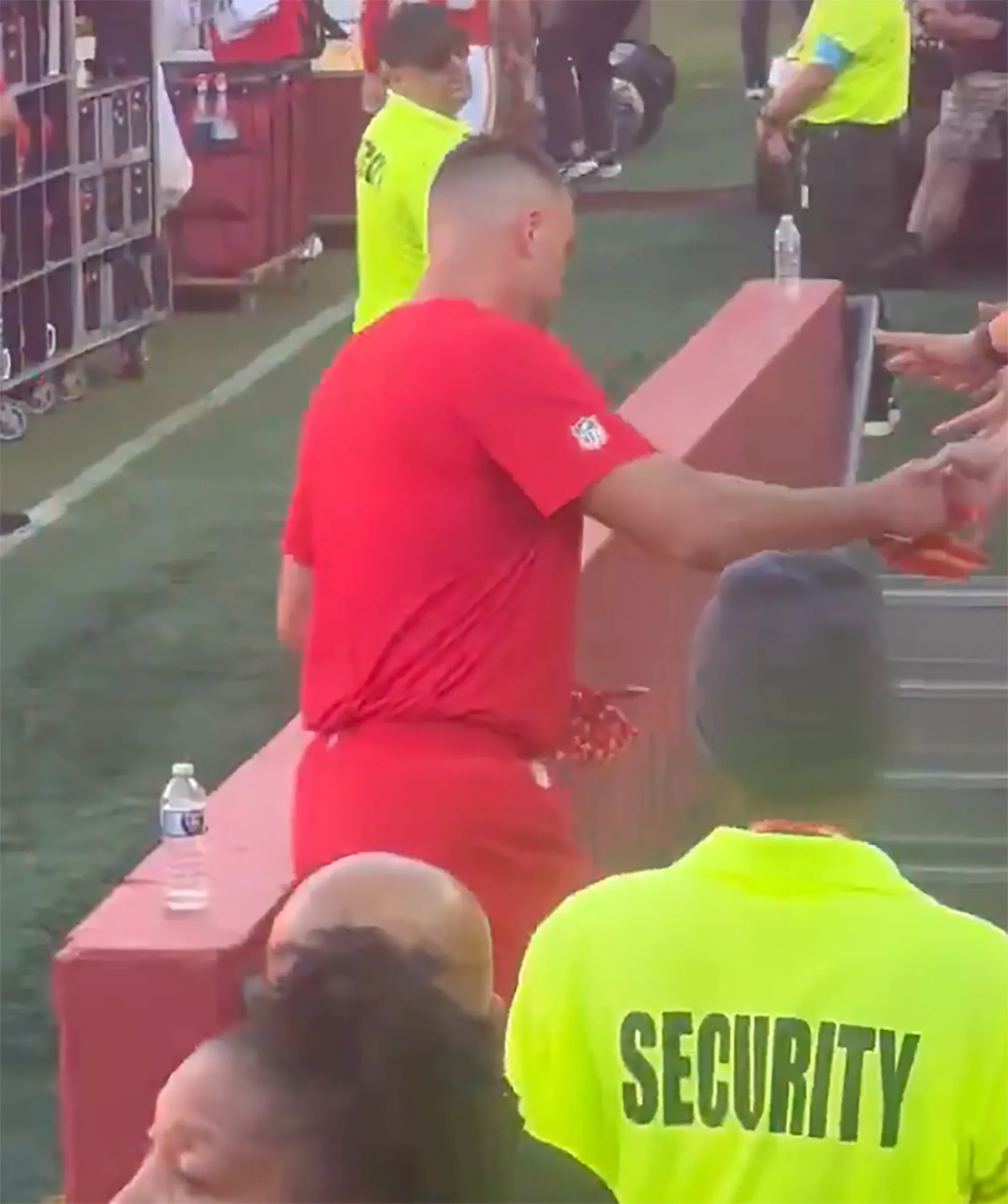 Travis Kelce, in a red t-shirt, giving high fives to fans.