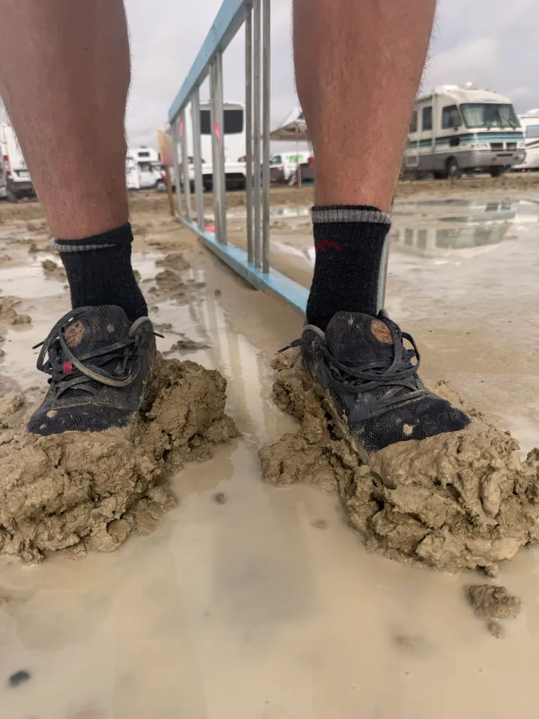 Person's muddy shoes and lower legs standing in flooded Black Rock City.