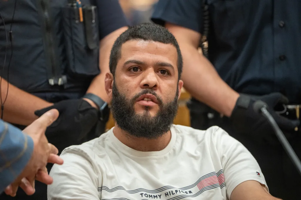 Yehia Amin in a white Tommy Hilfiger shirt, seated with law enforcement personnel around him.