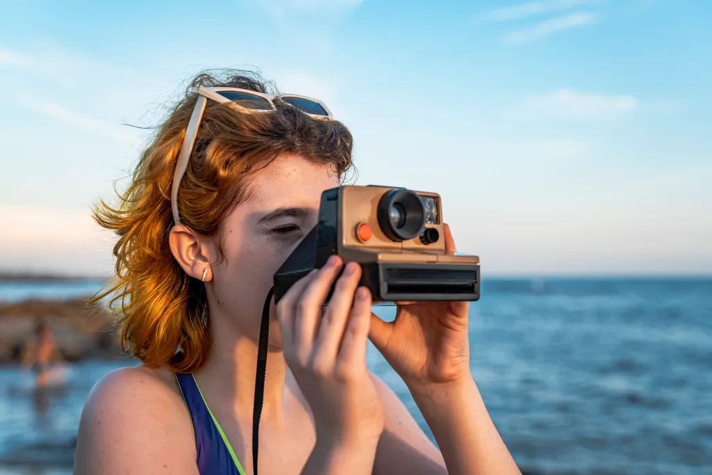 Young girl photographing a sunset over the sea with an old instant camera.