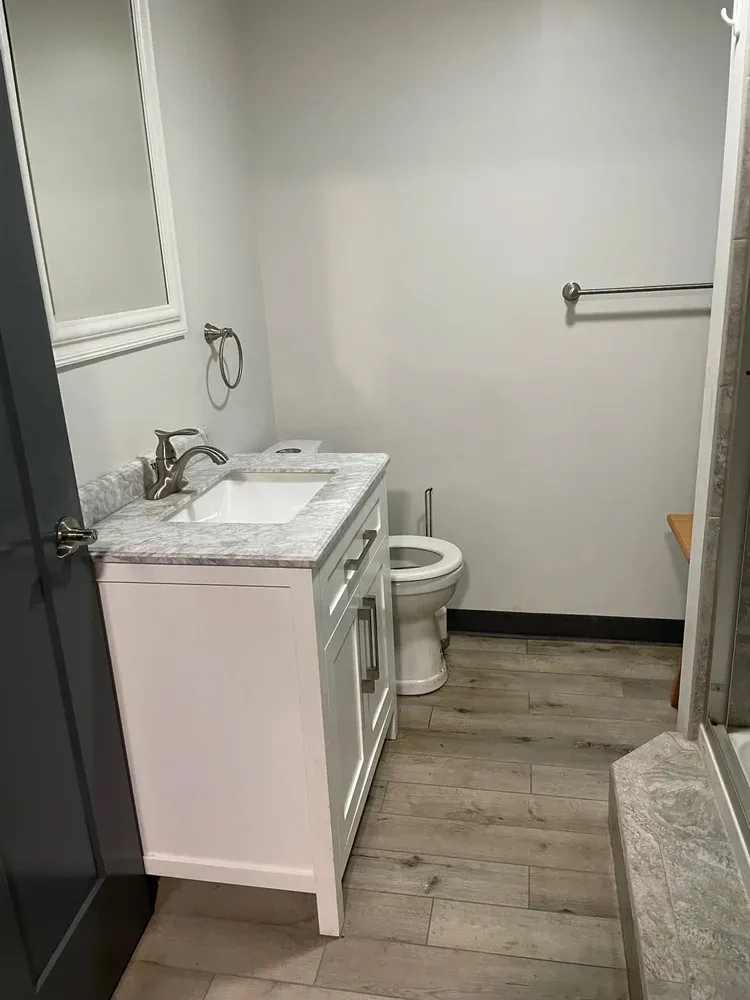 A clean and modern bathroom with a white vanity, marble countertop, and light wood-look tiled floor.