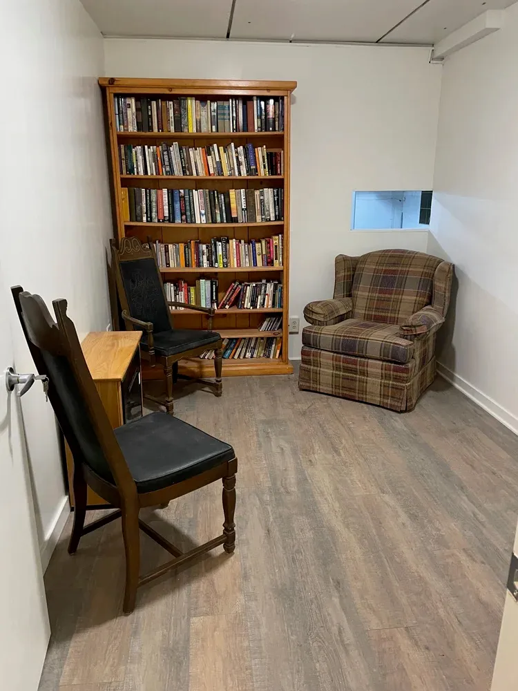 A room with a full bookshelf, a plaid armchair, and two wooden chairs.