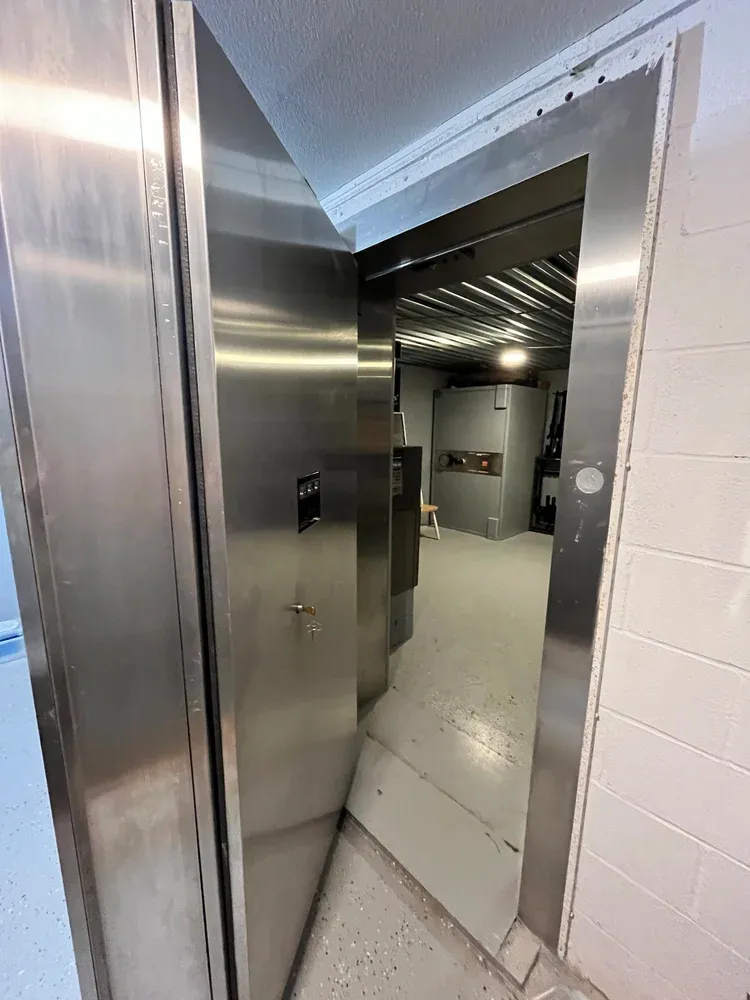 View into a bunker through a thick, open vault door, showing a second safe inside.