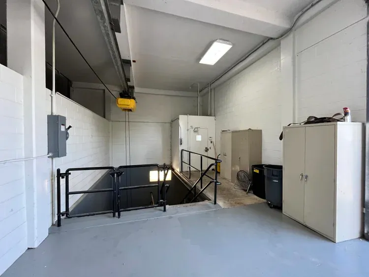 Entrance to a doomsday bunker with stairs leading down, a hoist above, and storage cabinets.