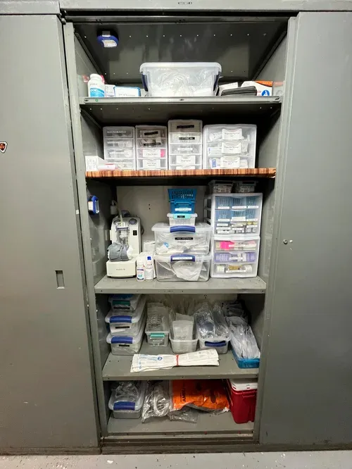 A metal cabinet filled with various medical supplies, organized in clear containers and bins.