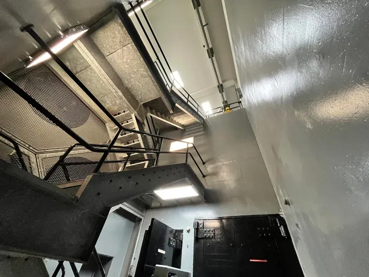 An interior view of a multi-story bunker with stairs, railings, and large metal doors.