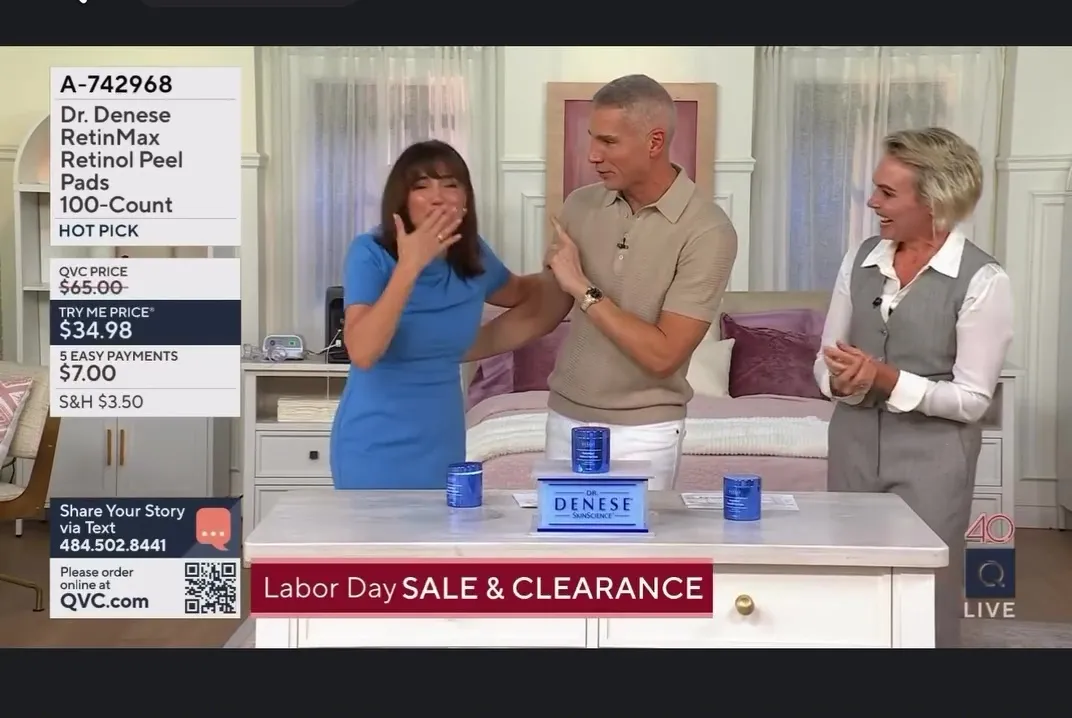 A female QVC presenter reacts emotionally to an on-screen reunion, while two co-hosts look on.
