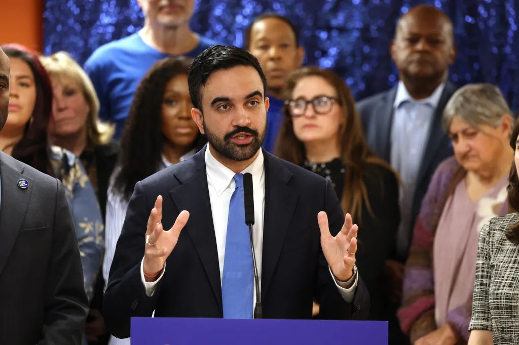 Mayor Zohran Mamdani speaks at a press conference, gesturing with his hands while standing at a podium.