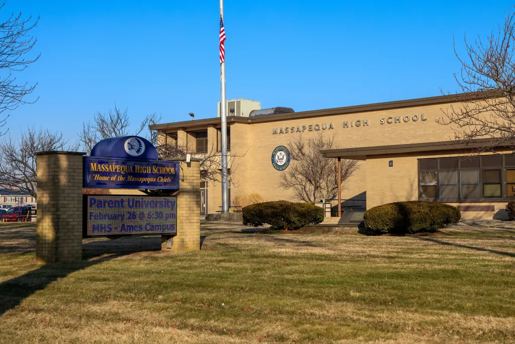 Exterior view of Massapequa High School with a sign in the foreground reading 