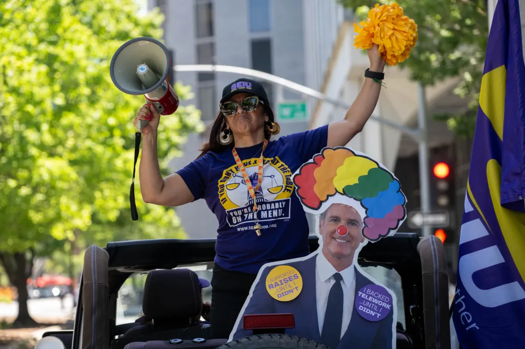 Anica Walls, president of SEIU Local 1000, holds a megaphone and raises a yellow pom-pom while standing in a vehicle during a protest against return-to-office requirements in Sacramento.