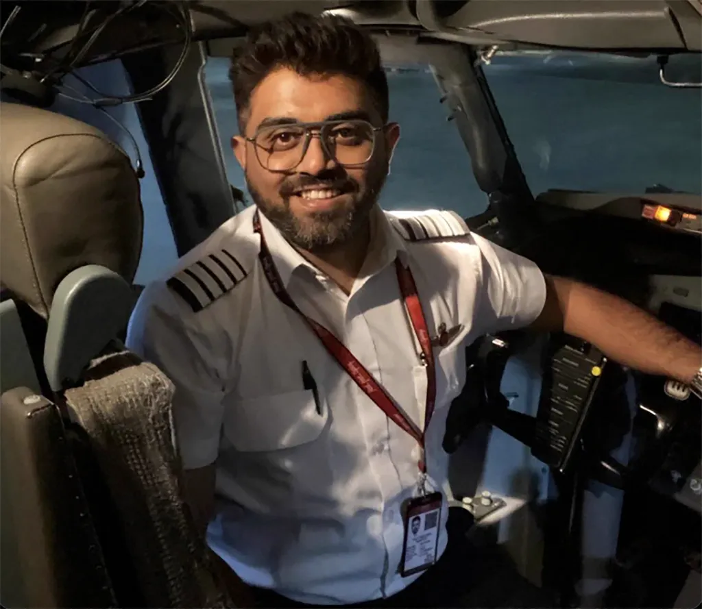 Indian pilot Smit Machchhar sitting in an airplane cockpit, smiling at the camera.