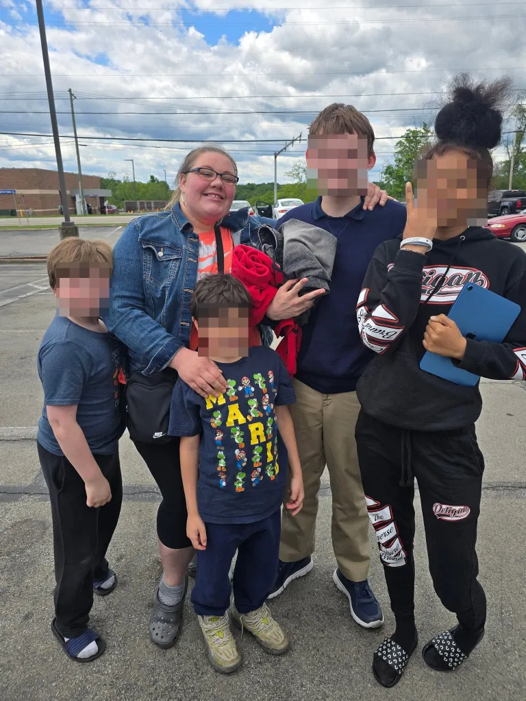 A mother and her four children pose for a photo in a parking lot.