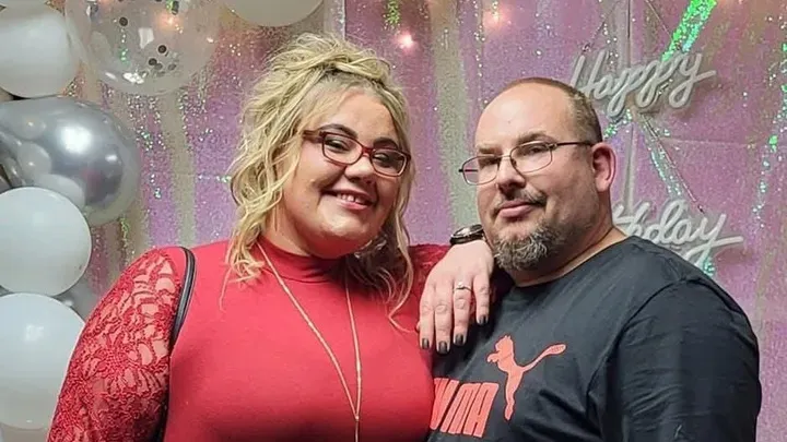 A smiling woman in a red dress with a man in a black t-shirt.