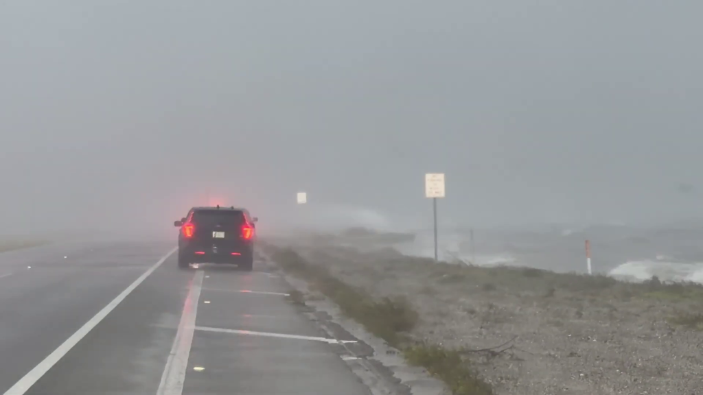 A car drives along a flooded coastal road as Hurricane Isaias approaches.
