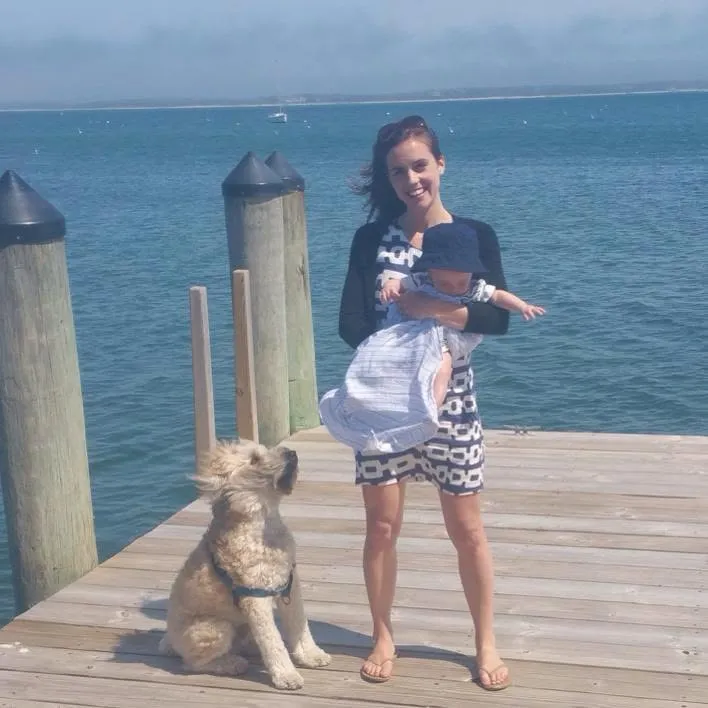 Kyle Kennedy standing on a wooden dock holding a baby while a dog sits beside them.