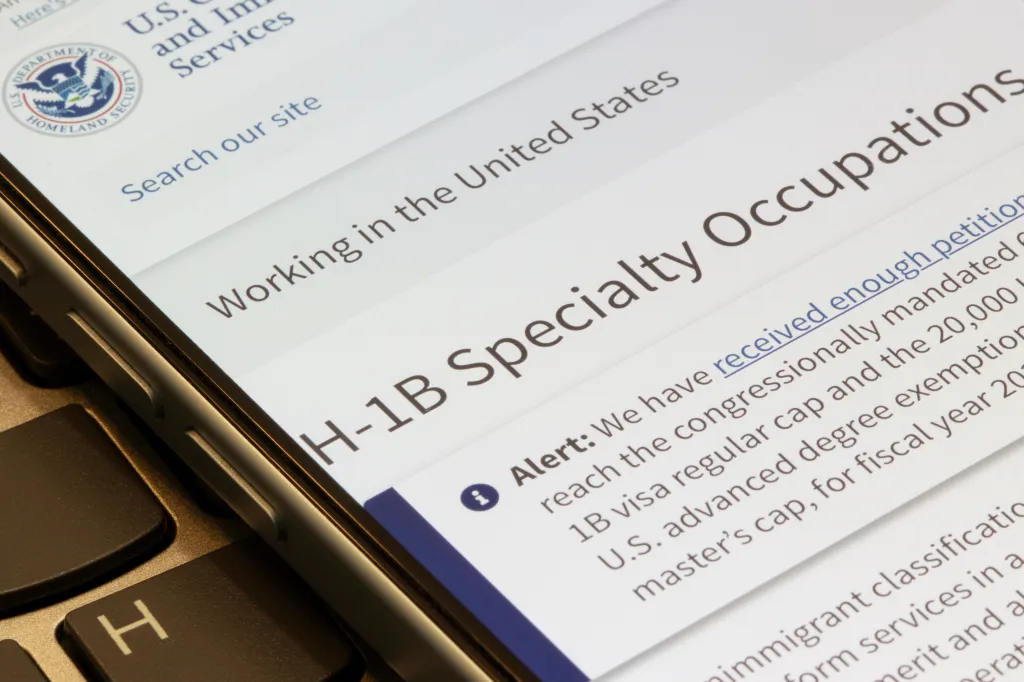 An iPhone displays the H-1B specialty occupations webpage from the official USCIS website.
