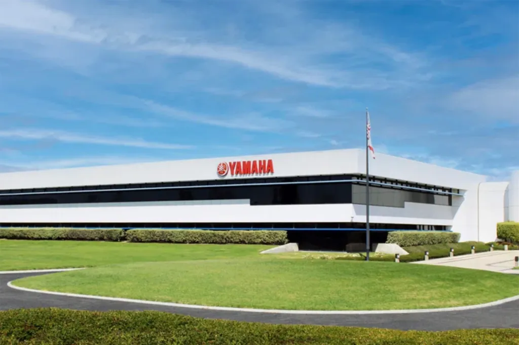 The Yamaha corporate headquarters building featuring a white exterior, large tinted windows, and a prominent red Yamaha logo on the front.