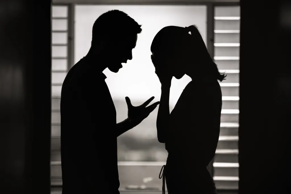 Silhouette of a man shouting at a crying woman covering her face, symbolizing domestic violence.