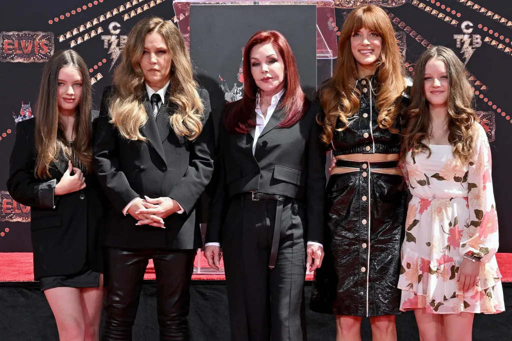 Priscilla Presley, Lisa Marie Presley, and Riley Keough stand with two other family members in front of a red carpet backdrop.