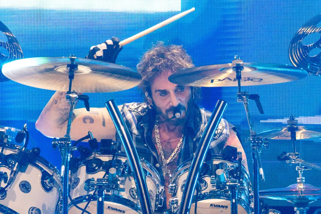 Drummer with a beard and a plaid shirt playing the drums on stage.