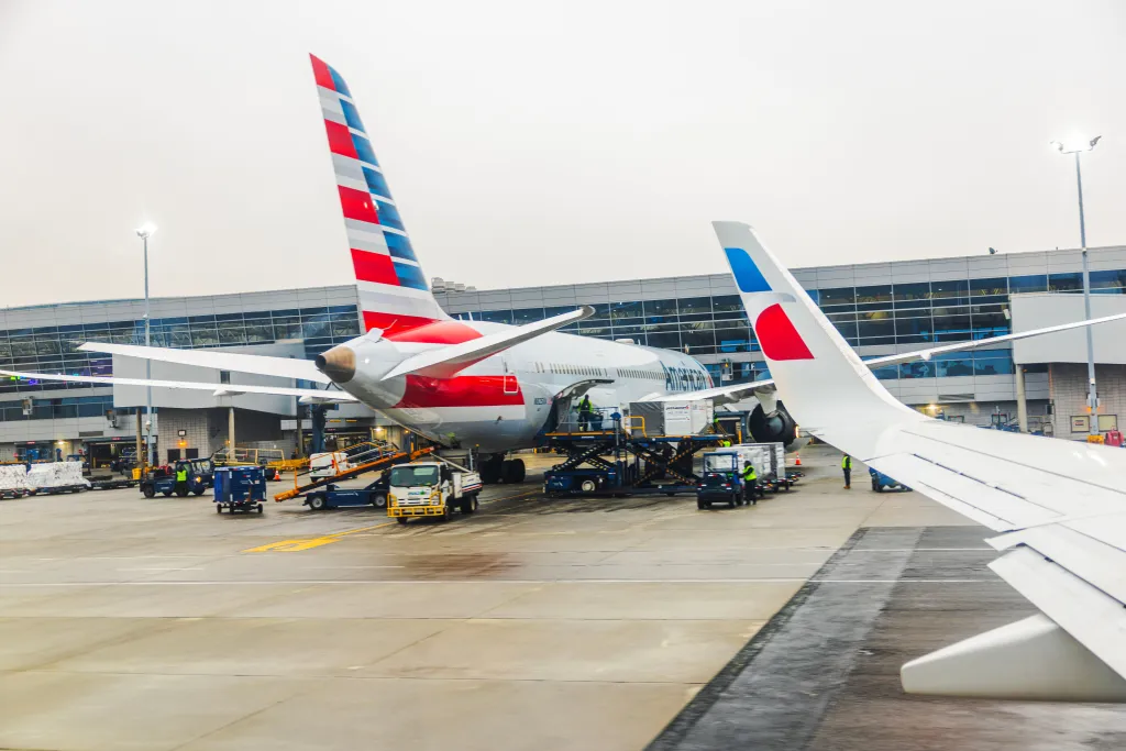 Ground crew loads an American Airlines aircraft at JFK airport in cloudy weather.