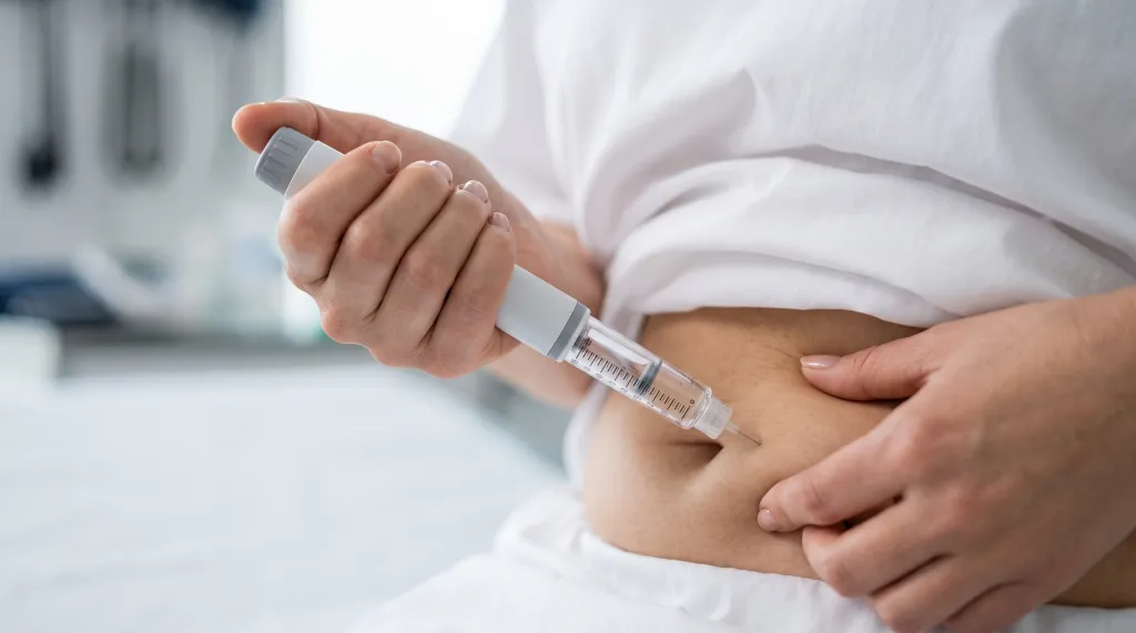 A person injecting insulin into their abdomen with an injection pen.