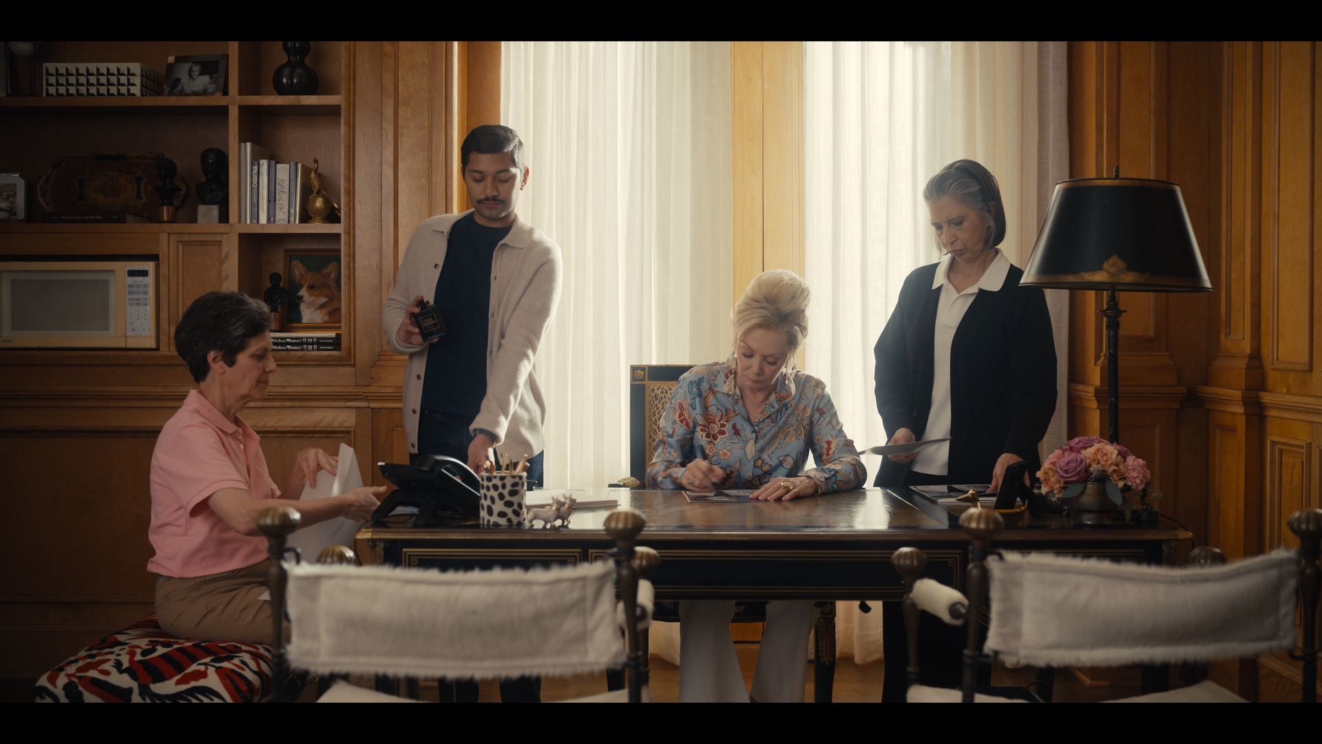 Jean Smart seated at a desk, surrounded by staff members in an office setting.