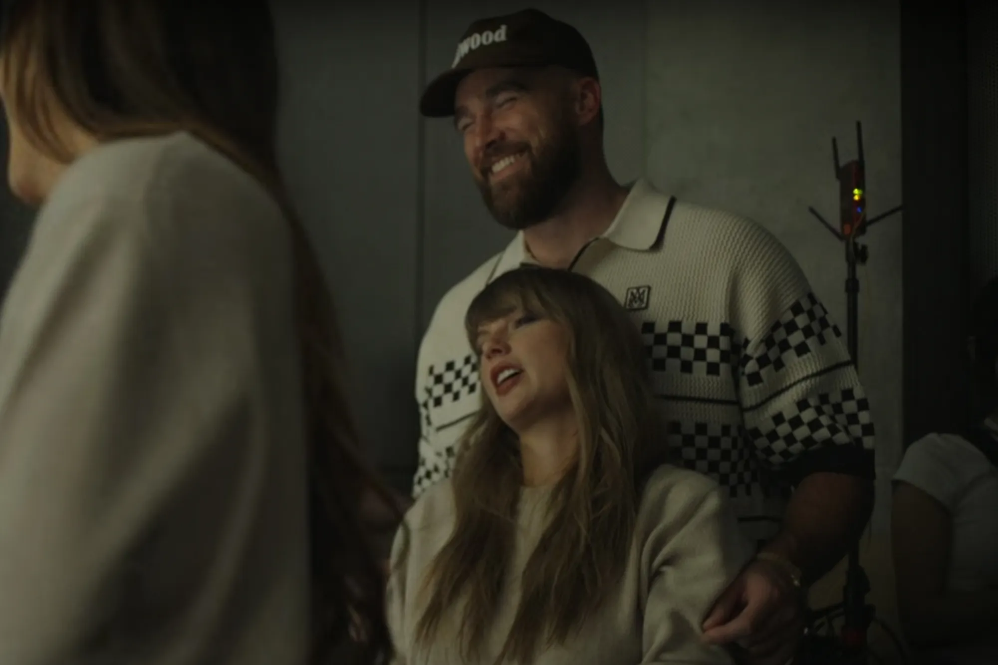 Travis Kelce smiling while standing behind Taylor Swift.