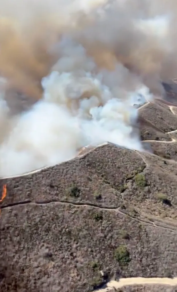 Aerial view of thick smoke and flames from the Norte Fire billowing over dry hillsides.