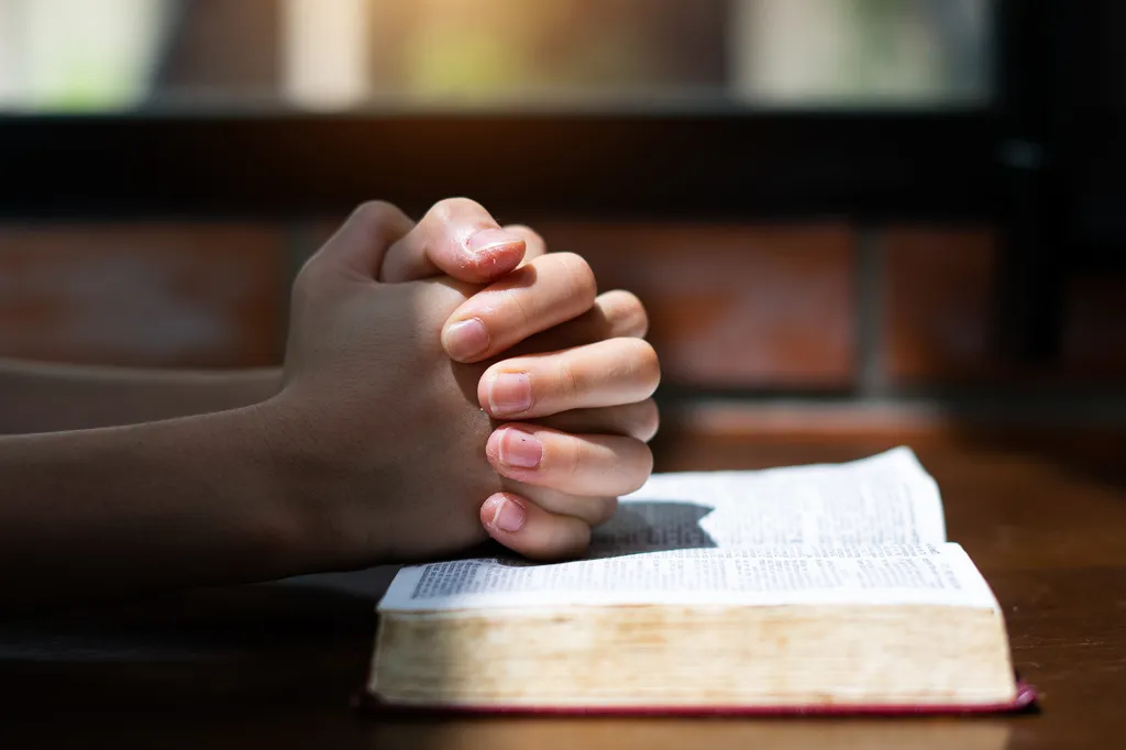 Hands clasped in prayer over an open Bible.
