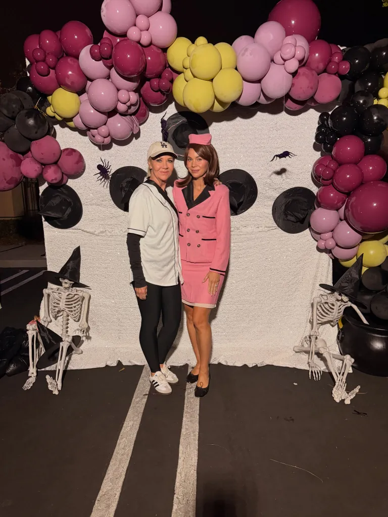 Two women pose for a photo in front of a Halloween backdrop.
