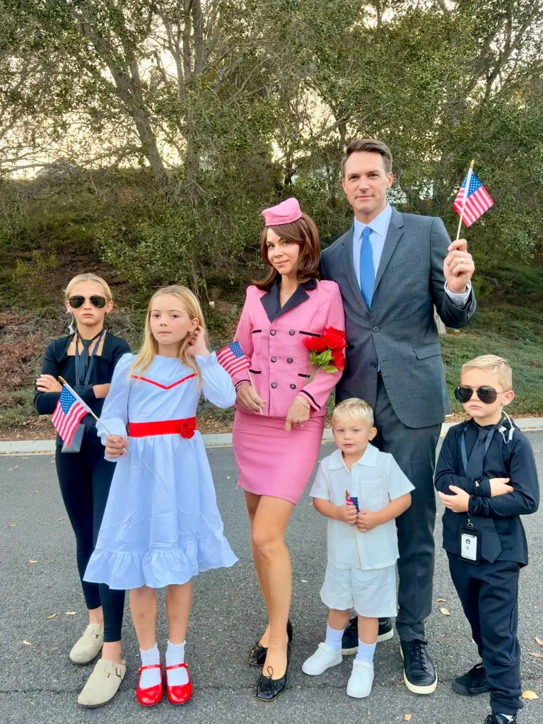 A family of six poses dressed as John F. Kennedy, Jacqueline Kennedy, and their children, holding American flags.