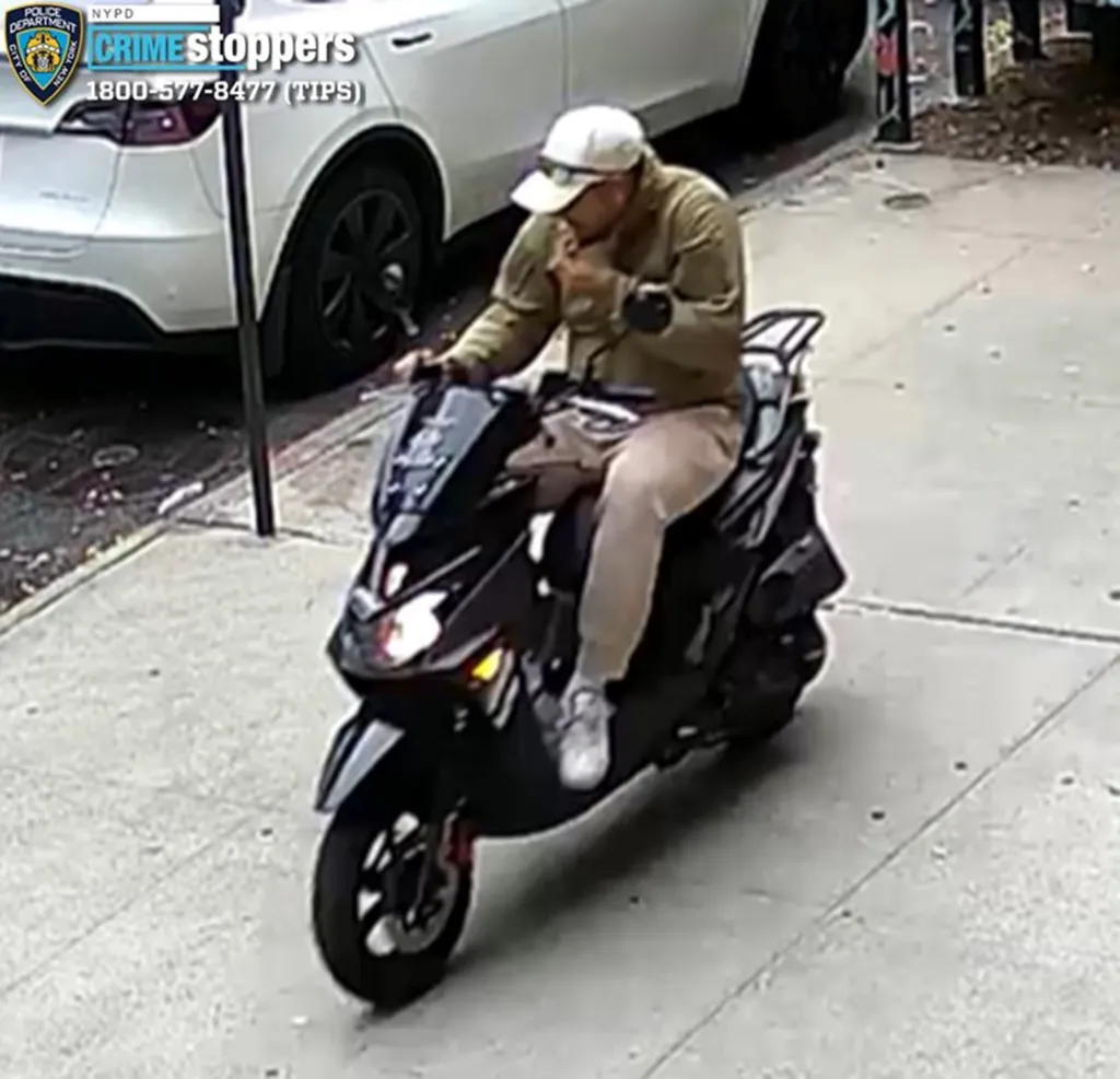 Surveillance photo of an unidentified individual wearing a white baseball cap, olive jacket, and light pants, riding a black moped.