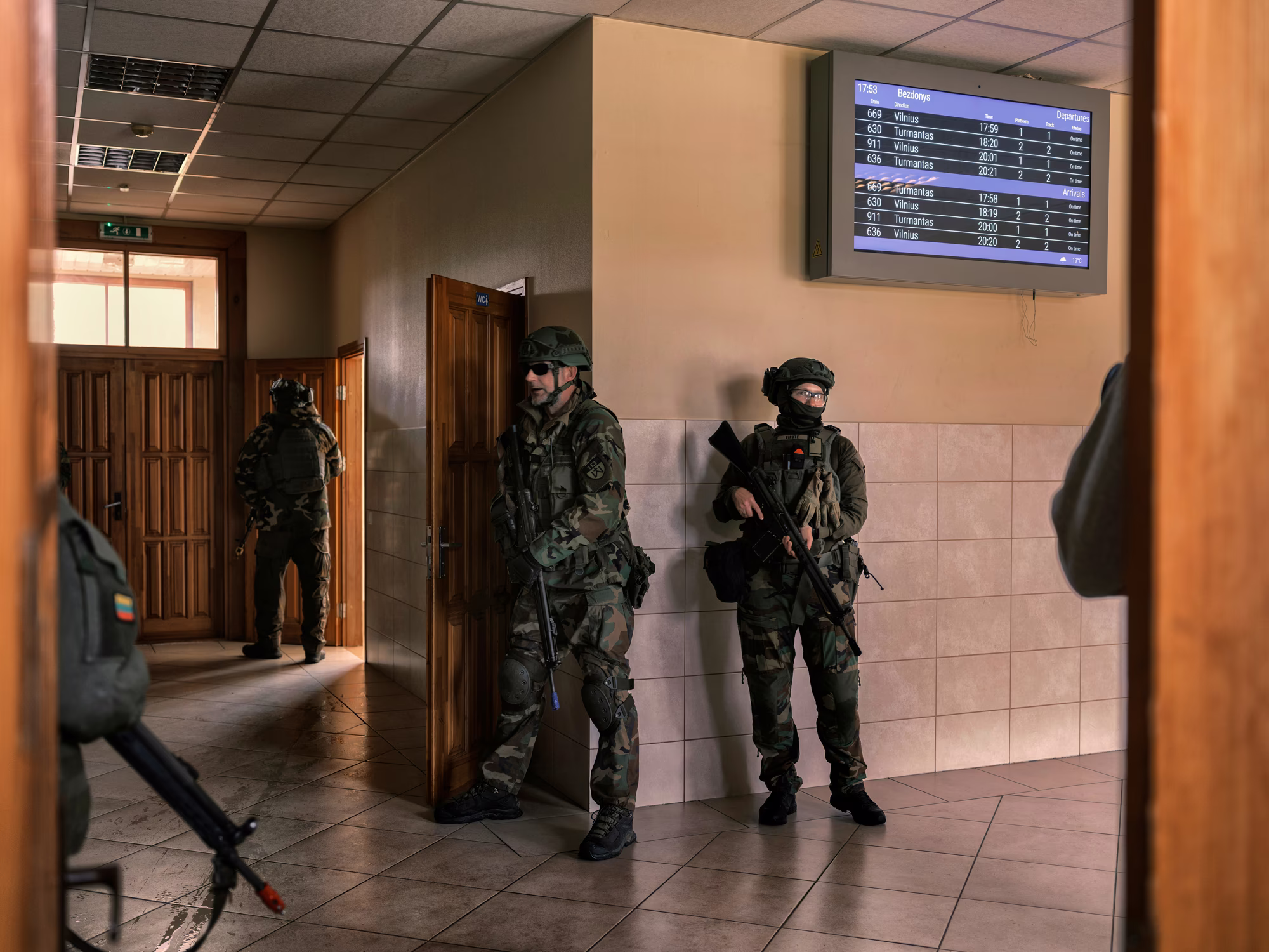 photo of heavily armed uniformed militia members inside train station with tiled-floor and departure sign