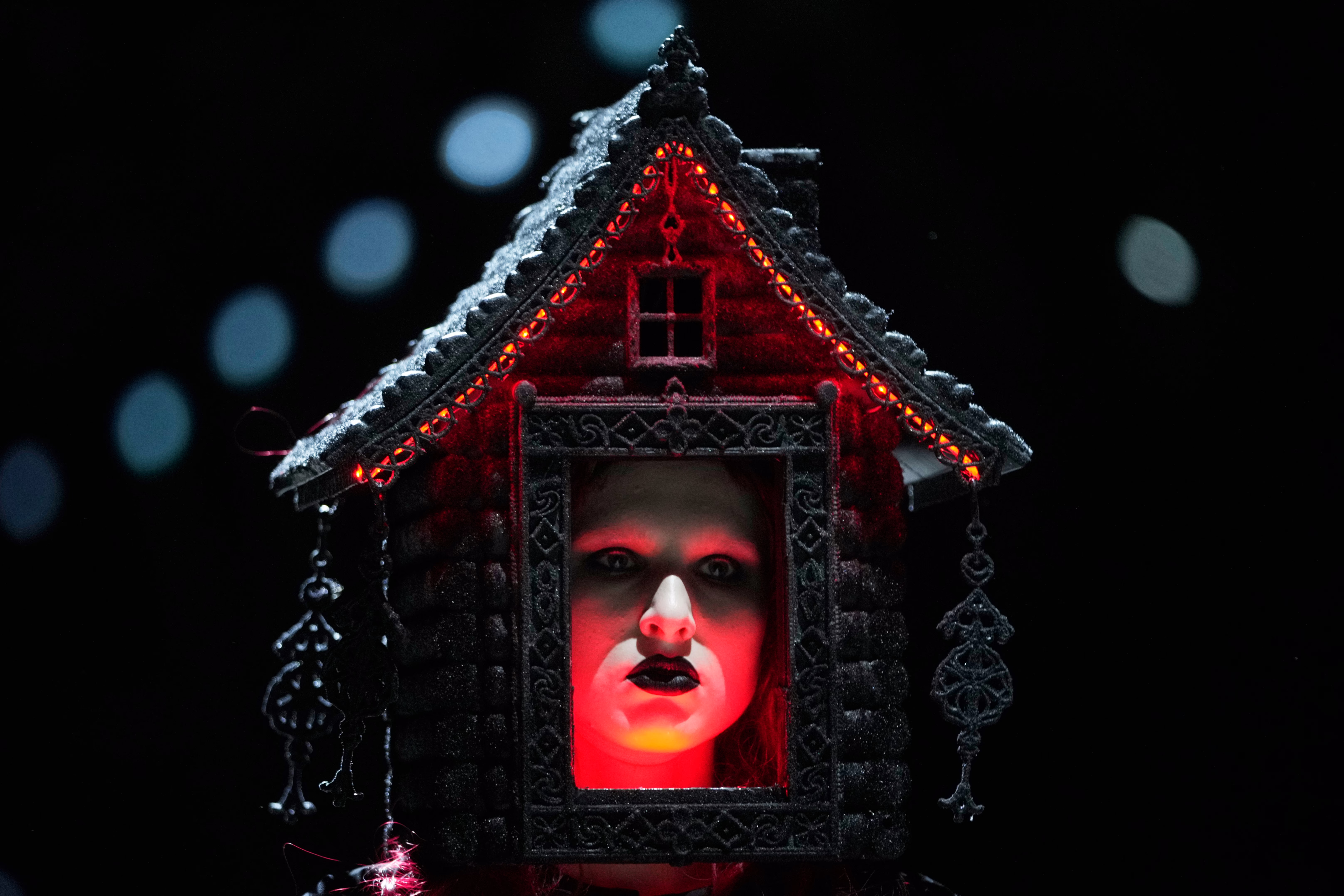 A model wears a fanciful house as a full-head adornment, their face visible through the front door.