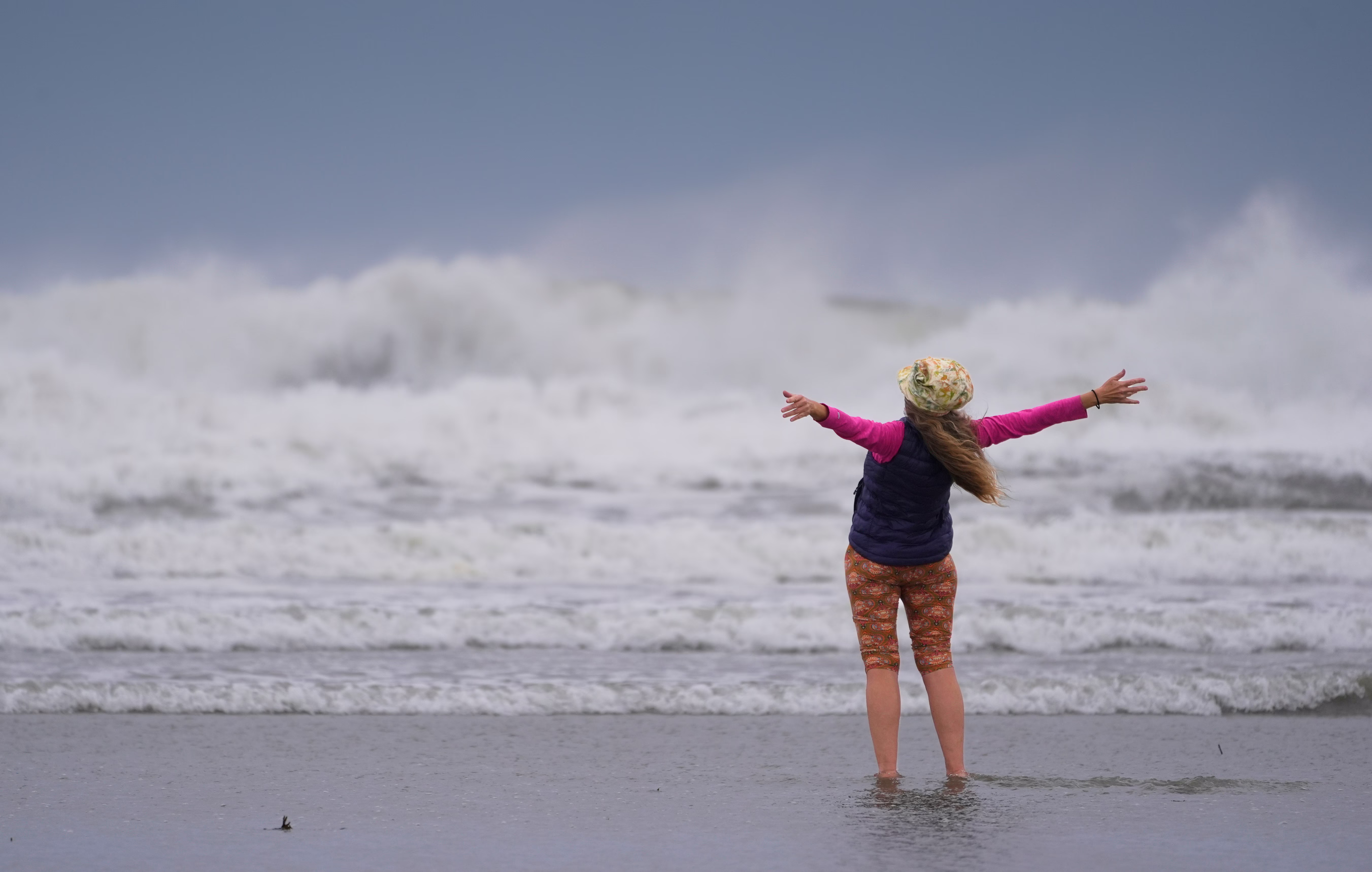 A person stands on a beach during a storm, facing the rough water, with arms wide open.