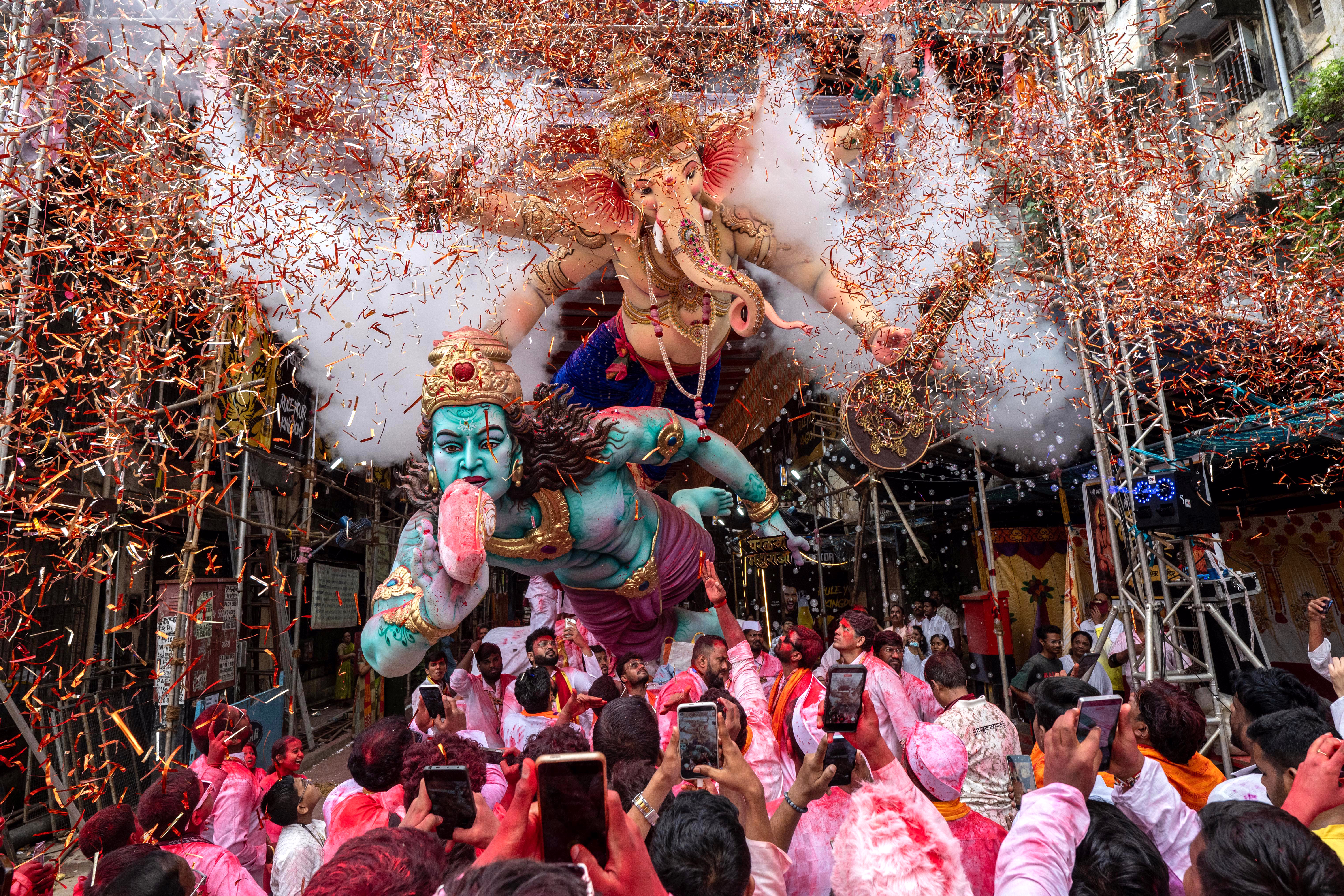 Devotees carry an idol of the Hindu deity Ganesha, as smoke and confetti fill the air.