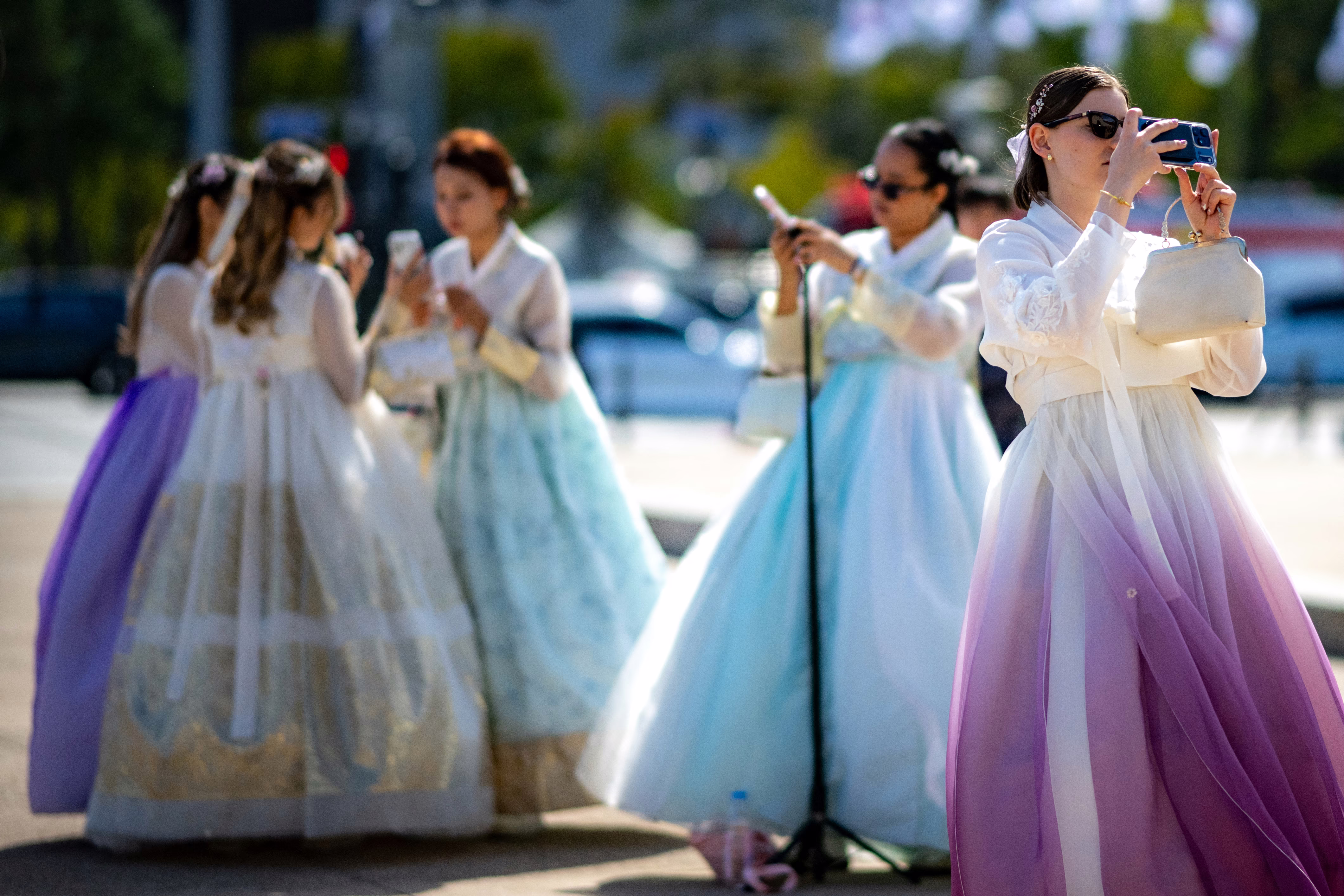 Tourists in traditional Hanbok outfits take photos outside a palace in Seoul.