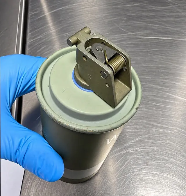 A gloved hand holds a spent M18 smoke grenade discovered in a passenger's carry-on bag at Watertown International Airport.