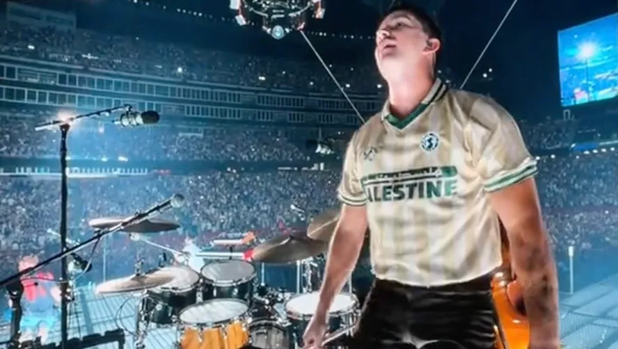 Zach Bryan's drummer wearing a Palestine jersey on stage during a concert in front of a large crowd.