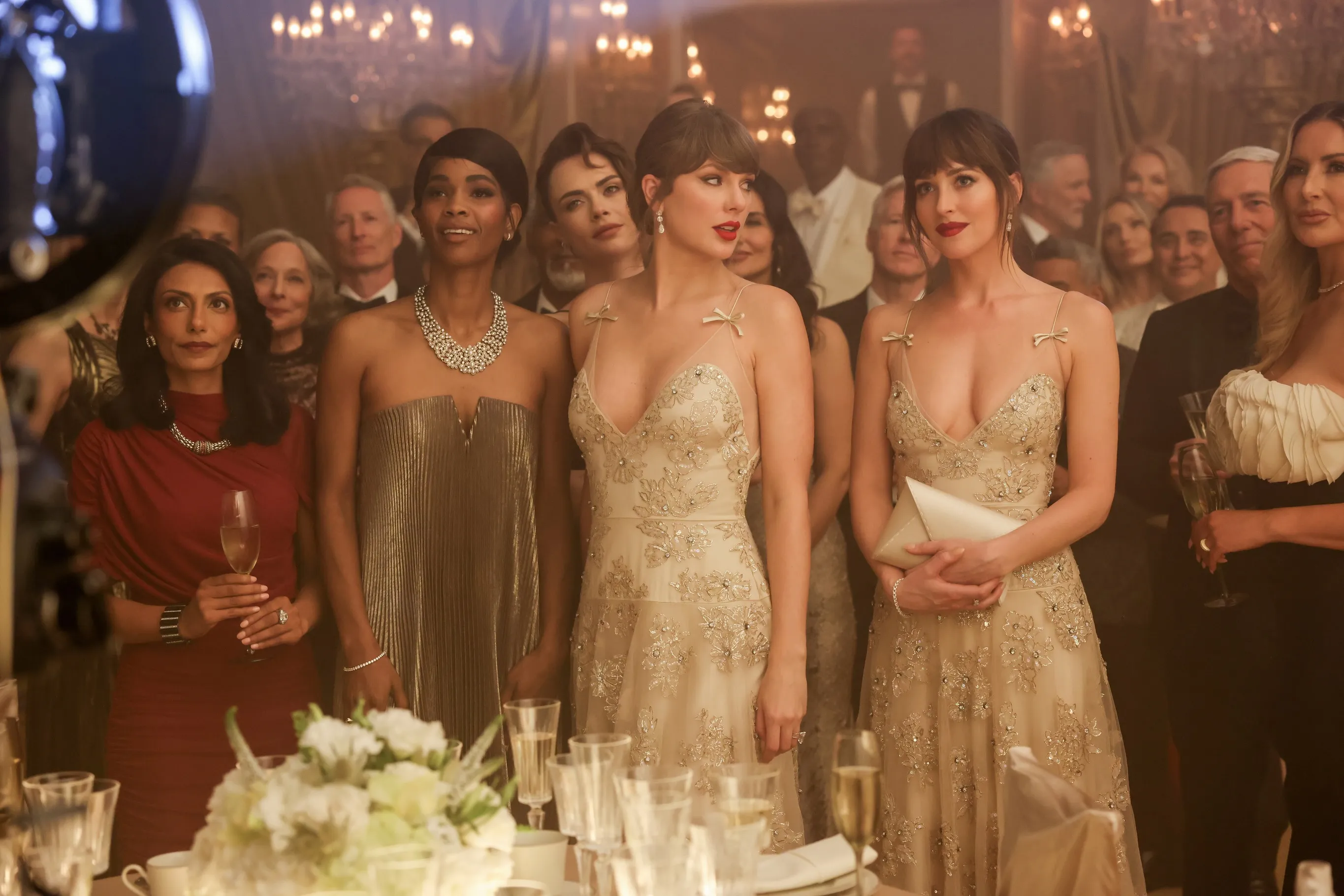 Taylor Swift and Dakota Johnson in identical beaded dresses with several other guests at a formal event.