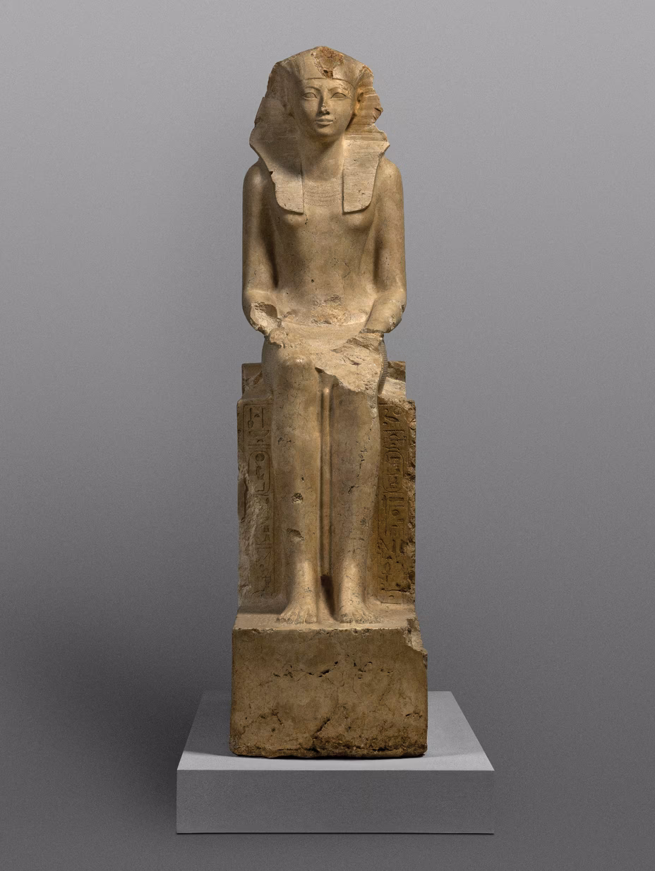 photo of stone sculpture of seated woman in Egyptian and pharaonic dress facing forward with hands in lap