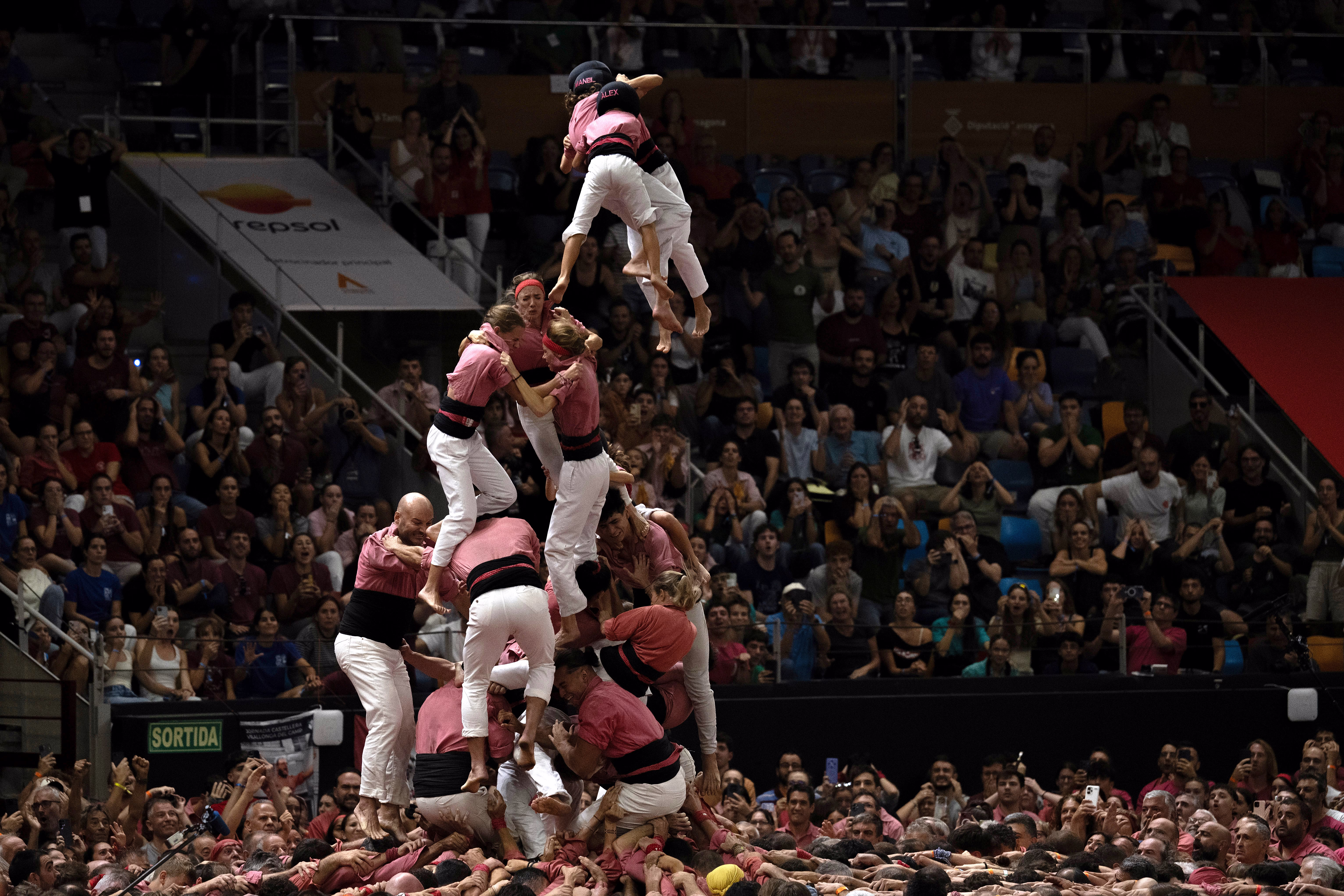 A partially-formed human tower collapses, with people falling toward their gathered team below.