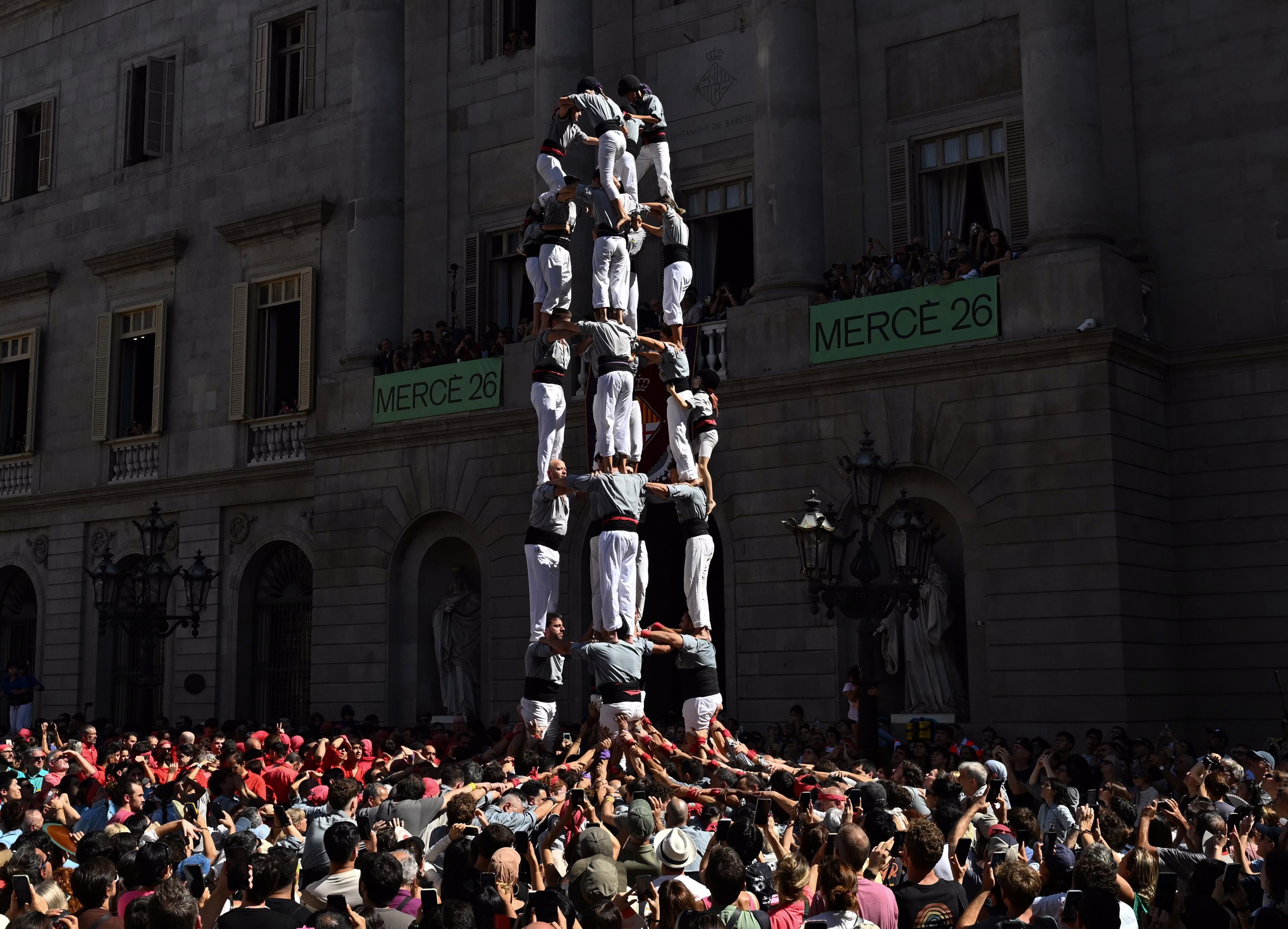 People watch as a human tower is formed, about six people tall.
