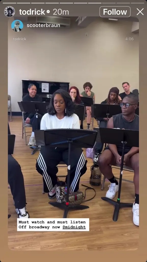 Scooter Braun and Todrick Hall seated with a group of people at a table in a rehearsal studio.